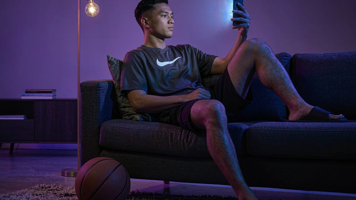 999JILI adult holding a phone with a basketball beside the sofa